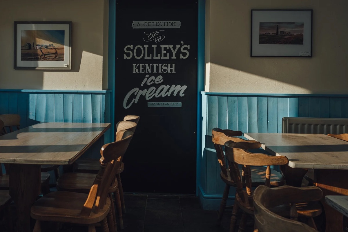 A sunlit seaside cafe with blue panelled walls and a chalkboard sign, photographed by Guillaume Flandre