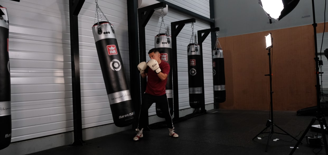 Boxer filming a heavy bag tutorial on a lit set in a gym
